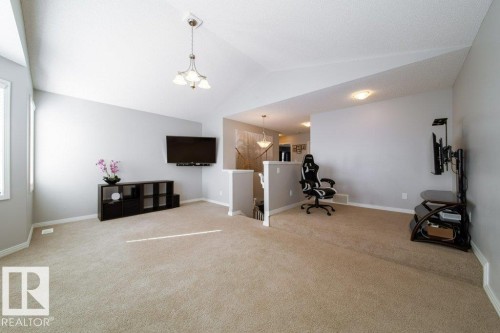 Vaulted ceiling with a pendant light fixture, wall-mounted television, neutral wall color, and carpeted flooring - 16120 138 Street Nw, Edmonton, AB 