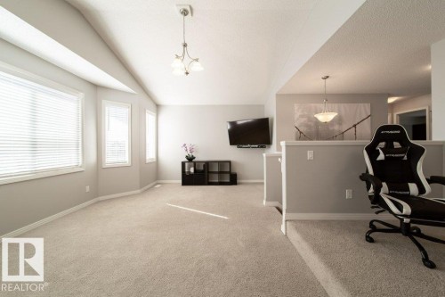 Vaulted ceiling with a decorative chandelier, multiple windows with horizontal blinds, neutral carpeting, and a half-wall partition - 16120 138 Street Nw, Edmonton, AB 