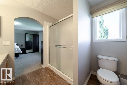 Wood-finish flooring, glass-enclosed shower, white toilet, and an arched doorway - 16120 138 Street Nw, Edmonton, AB 