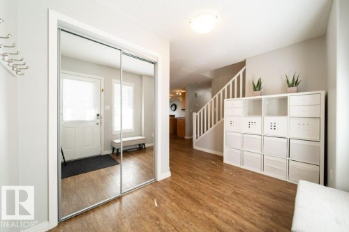 Wood-finish flooring throughout, mirrored sliding closet doors, a white front entry door with a privacy blind, and a staircase with white risers and railings - 16120 138 Street Nw, Edmonton, AB 