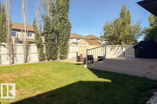 Expansive backyard featuring a tiered deck with white railings, a manicured lawn, perimeter fencing, mature trees, and a storage shed - 16120 138 Street Nw, Edmonton, AB 