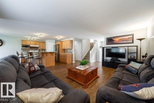 Open-concept living area featuring wood-finish flooring, a kitchen with light wood cabinetry, a breakfast bar, and stainless steel appliances - 16120 138 Street Nw, Edmonton, AB 