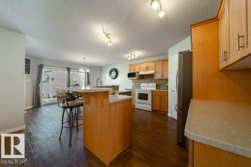 Kitchen featuring wood-finish cabinetry, light countertops, dark wood-finish flooring, and stainless steel appliances - 16120 138 Street Nw, Edmonton, AB 