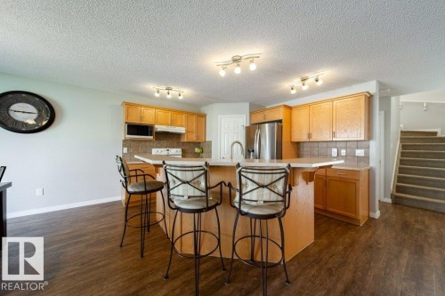 Kitchen featuring wood-finish cabinetry, stainless steel appliances, a tiled backsplash, and an island with bar seating - 16120 138 Street Nw, Edmonton, AB 