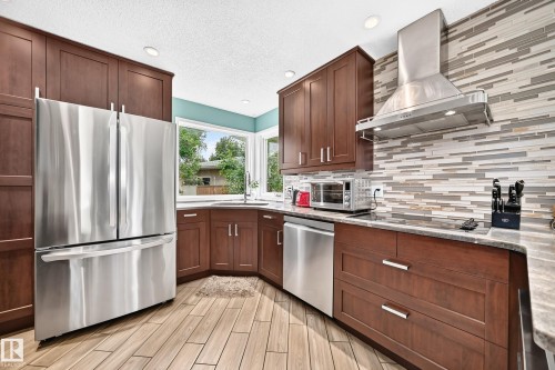 Kitchen featuring wood-finish flooring, dark wood cabinetry, stainless steel appliances, and a tiled backsplash - 8224 186 Street Nw, Edmonton, AB 