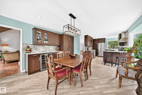 Spacious kitchen and dining area featuring wood-finish flooring, dark wood cabinetry, stainless steel appliances, a tile backsplash, and an island with bar seating - 8224 186 Street Nw, Edmonton, AB 