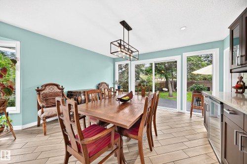 Wood-finish tile flooring, a modern linear chandelier, and expansive sliding glass doors providing outdoor access - 8224 186 Street Nw, Edmonton, AB 