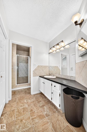 Tiled flooring, white vanity with integrated sink, dark countertop, mirrored wall, and a glass-enclosed shower - 8224 186 Street Nw, Edmonton, AB 