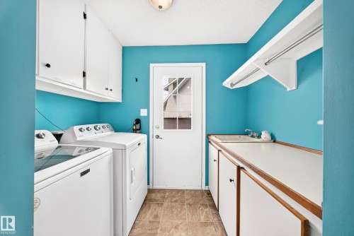 Dedicated laundry area featuring a utility sink, upper cabinetry, lower cabinetry, and a drying rack - 8224 186 Street Nw, Edmonton, AB 