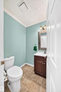 Powder room featuring a single vanity with a white countertop, under-sink cabinetry, a toilet, and tile flooring - 