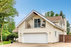 Two-car garage, upper balcony with sliding glass door, dormer windows, and light-colored siding - 