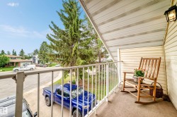 Balcony featuring slatted siding, a white metal railing, and an exterior wall light - 