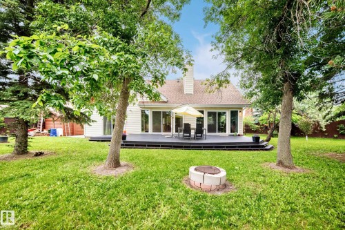 Expansive backyard featuring a manicured lawn, established trees, a paver and block fire pit, and a composite deck with sliding glass doors - 8224 186 Street Nw, Edmonton, AB 