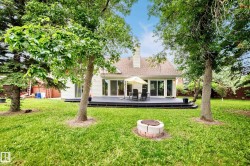Expansive backyard featuring a manicured lawn, established trees, a paver and block fire pit, and a composite deck with sliding glass doors - 