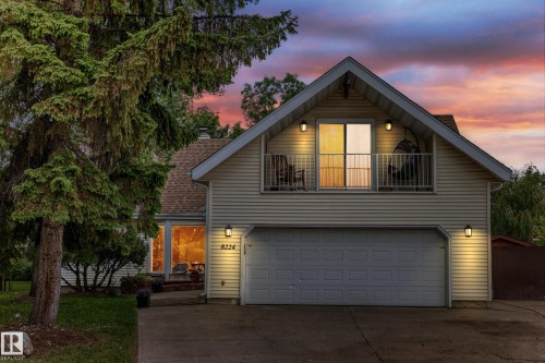 Gable roofline, white siding exterior, upper-level balcony with sliding glass door, attached two-car garage, and exterior wall-mounted lighting - 8224 186 Street Nw, Edmonton, AB 