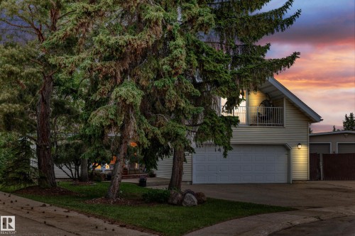 Attached two-car garage, upper balcony with railing, siding exterior, mature trees, and a paved driveway - 8224 186 Street Nw, Edmonton, AB 