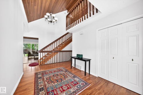 Foyer featuring wood-finish flooring, a wood-paneled vaulted ceiling, a chandelier, and a wood staircase with banister - 8224 186 Street Nw, Edmonton, AB 