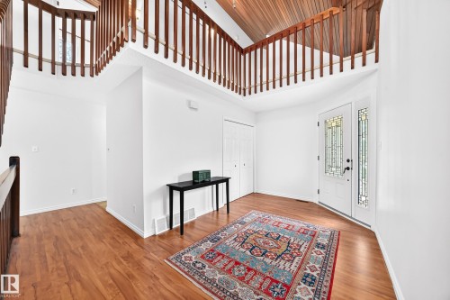 Entryway featuring wood-finish flooring, a white paneled front door with decorative glass, and a vaulted wood-paneled ceiling with an upper-level railing - 8224 186 Street Nw, Edmonton, AB 