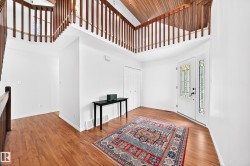 Entryway featuring wood-finish flooring, a white paneled front door with decorative glass, and a vaulted wood-paneled ceiling with an upper-level railing - 