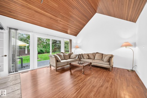 Vaulted wood-paneled ceiling, wood-finish flooring, white walls, and glass sliding doors opening to a patio and grassy area - 8224 186 Street Nw, Edmonton, AB 