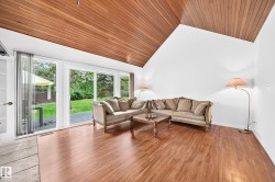 Vaulted wood-paneled ceiling, wood-finish flooring, white walls, and glass sliding doors opening to a patio and grassy area - 