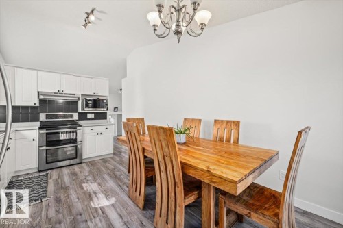 Kitchen and dining area featuring white cabinetry, stainless steel appliances, dark tile backsplash, and wood-finish flooring - 40 Hampton Place, Stony Plain, AB 
