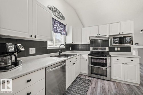 White cabinetry with black hardware, black tiled backsplash, stainless steel appliances, and wood-finish flooring - 40 Hampton Place, Stony Plain, AB 