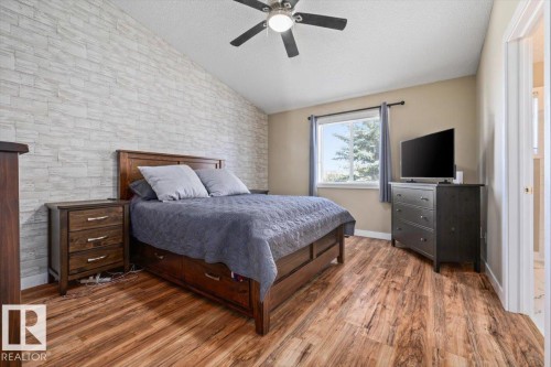 Vaulted ceiling with a ceiling fan, accent wall featuring light-toned stacked stone, wood-finish flooring, and a large window - 40 Hampton Place, Stony Plain, AB 