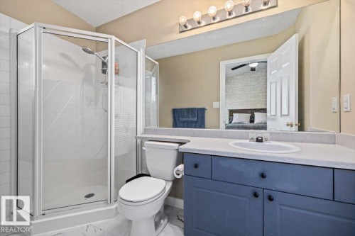 White-framed glass shower enclosure, single vanity with integrated sink, blue cabinet base, light-toned countertop, and overhead vanity lighting - 40 Hampton Place, Stony Plain, AB 