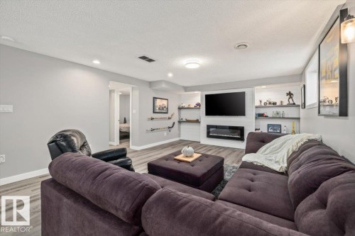 Wood-finish flooring with recessed lighting, built-in shelving, an integrated wall-mounted fireplace, and light gray wall paint - 40 Hampton Place, Stony Plain, AB 