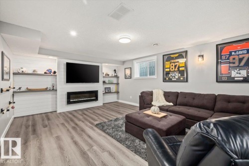 Integrated electric fireplace within a custom media wall, wood-finish flooring, recessed lighting, and a window with frosted glass - 40 Hampton Place, Stony Plain, AB 