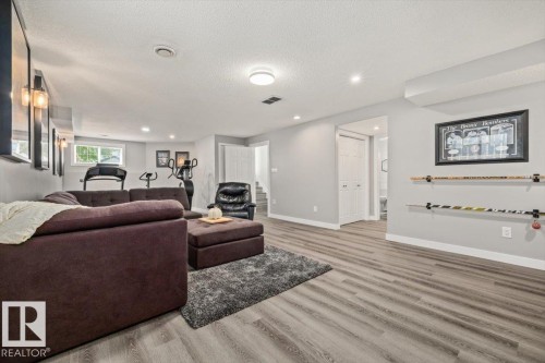 Spacious room featuring wood-finish flooring, recessed lighting, wall-mounted sconces, and a window providing natural illumination - 40 Hampton Place, Stony Plain, AB 