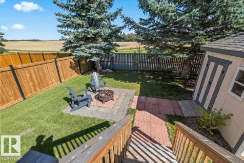 Green lawn area with a wood privacy fence, storage shed, and a paver patio featuring a fire pit - 40 Hampton Place, Stony Plain, AB 