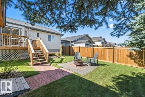 Expansive backyard featuring a wood deck with stairs, a paver patio, brick pathway, and a wood fence - 40 Hampton Place, Stony Plain, AB 
