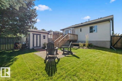 Expansive backyard featuring a manicured lawn, a raised wood deck with staircase, a storage shed, and a paved patio area - 40 Hampton Place, Stony Plain, AB 