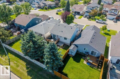 Expansive fenced backyard with mature evergreen trees, a wooden deck, and a storage shed - 40 Hampton Place, Stony Plain, AB 
