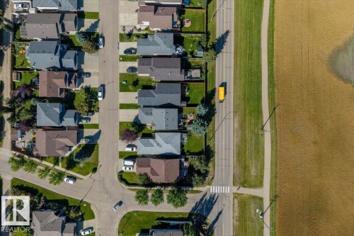 Aerial perspective showcasing residential properties with gray and brown roofs, green lawns, and a paved road with a sidewalk - 40 Hampton Place, Stony Plain, AB 