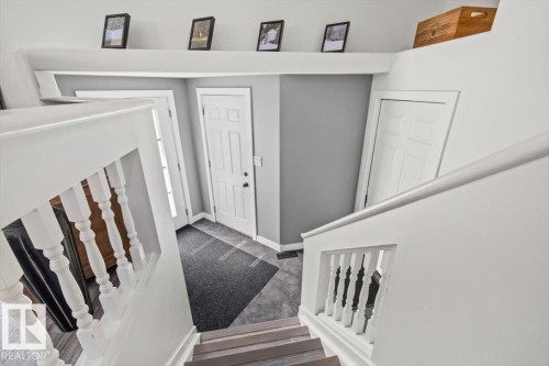 White painted stair railing with turned balusters, wood-finish stair treads, and a white paneled door - 40 Hampton Place, Stony Plain, AB 