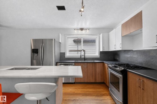 Kitchen featuring a two-toned cabinetry, stainless steel appliances, dark countertops, and a central island with a built-in sink - 17103 92 Street Nw, Edmonton, AB 