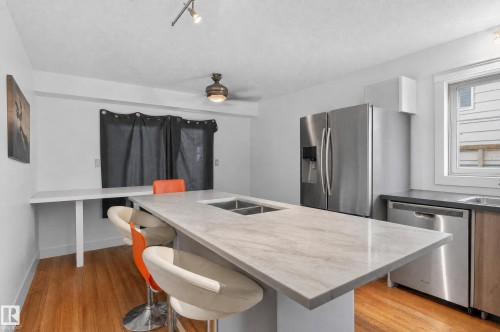 Kitchen featuring a double basin sink, stainless steel appliances, wood-finish flooring, and a large central island with seating - 17103 92 Street Nw, Edmonton, AB 