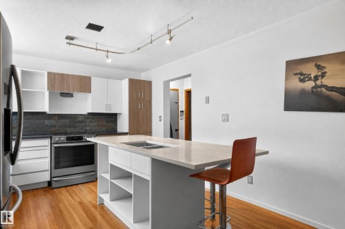 Kitchen featuring wood-finish flooring, white cabinetry with wood-tone accents, stainless steel appliances, and a central island with an integrated sink and light-toned countertop - 17103 92 Street Nw, Edmonton, AB 
