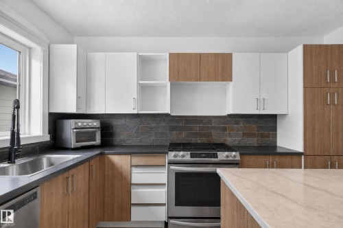 Modern kitchen with two-tone cabinetry, stainless steel appliances, dark stone-look backsplash, and light-toned countertops - 17103 92 Street Nw, Edmonton, AB 