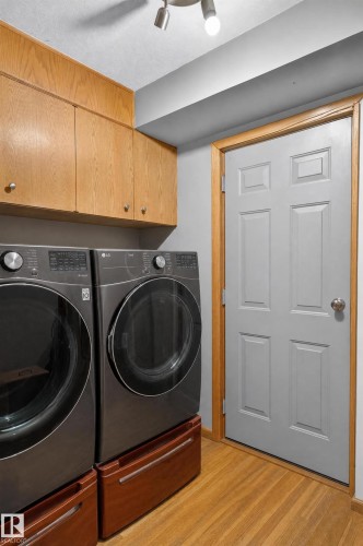 Integrated laundry appliances with elevated pedestals, upper cabinetry, and wood-finish flooring - 17103 92 Street Nw, Edmonton, AB 