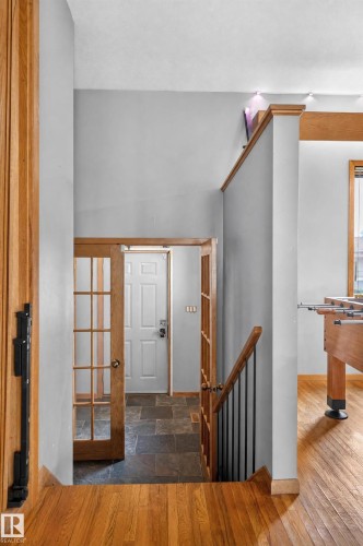 Wood-finish flooring, staircase with wood handrail and black metal balusters, French doors with glass panels, slate tile flooring, and a white paneled door - 17103 92 Street Nw, Edmonton, AB 