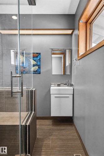 Modern bathroom featuring a floating vanity with integrated sink, a glass-enclosed shower, and wood-finish tile flooring - 17103 92 Street Nw, Edmonton, AB 