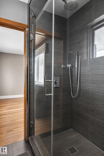 Glass-enclosed shower with dark tile surround, integrated shower drain, and rain showerhead - 17103 92 Street Nw, Edmonton, AB 