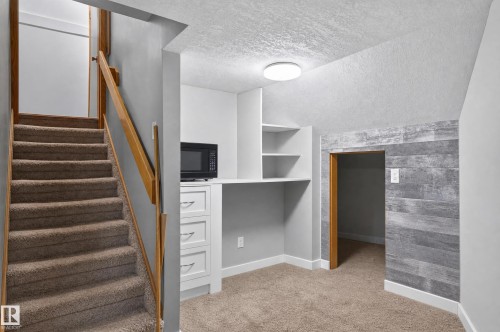Carpeted staircase with wooden handrail, built-in desk with shelving, custom cabinetry with drawers, and plank-style accent wall - 17103 92 Street Nw, Edmonton, AB 