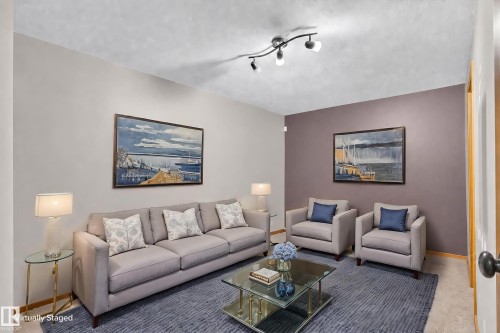 Track lighting fixtures illuminate the living area featuring neutral wall tones and a distinct accent wall - 17103 92 Street Nw, Edmonton, AB 