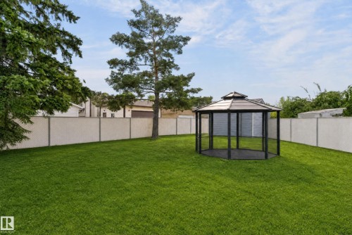 Expansive grassy yard featuring a dark-framed gazebo with a tiered roof, a mature tree, and perimeter fencing - 17103 92 Street Nw, Edmonton, AB 
