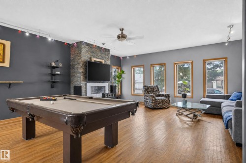 Wood-finish flooring, a stone-accented fireplace, built-in shelving, track lighting, and multiple windows - 17103 92 Street Nw, Edmonton, AB 